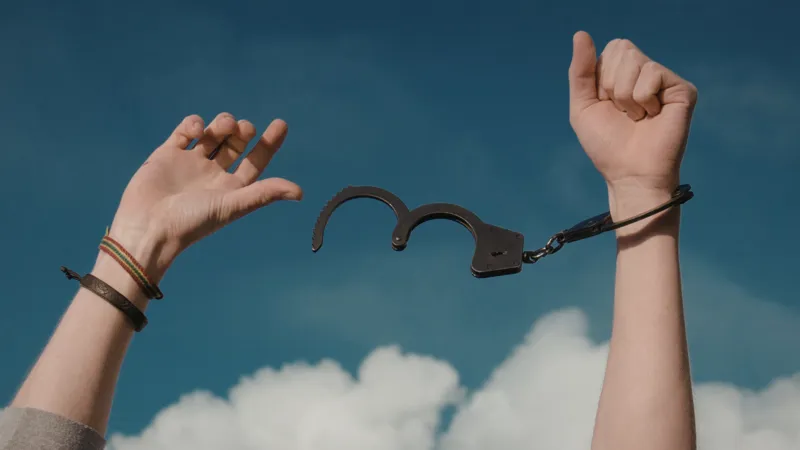 Hands Breaking Free From Handcuffs Against A Blue Sky